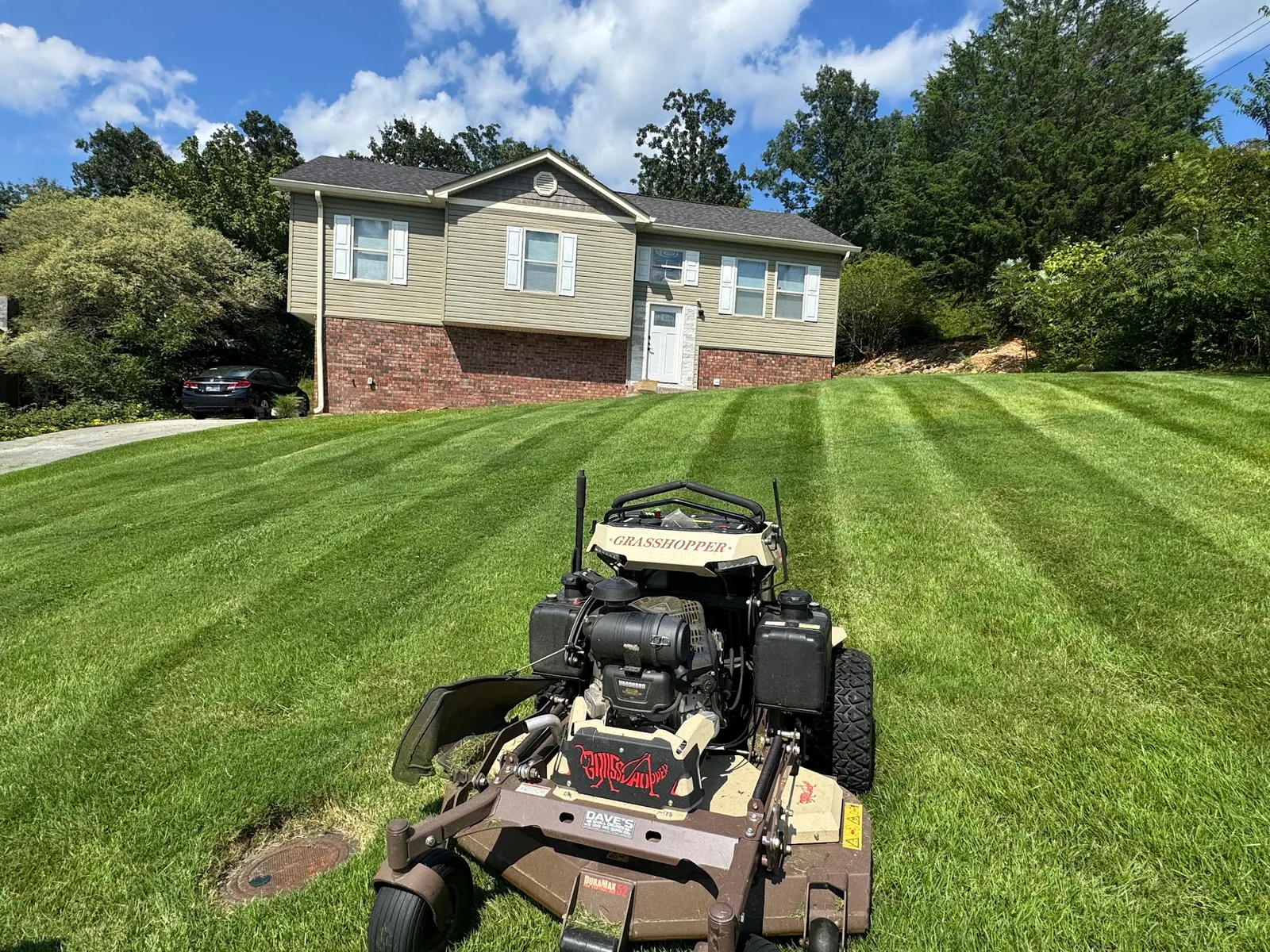 Stand-on mower parked on a freshly striped lawn in front of a two-story home
