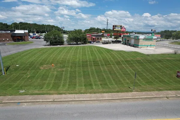 Large open lot mowed in even stripes beside a commercial strip