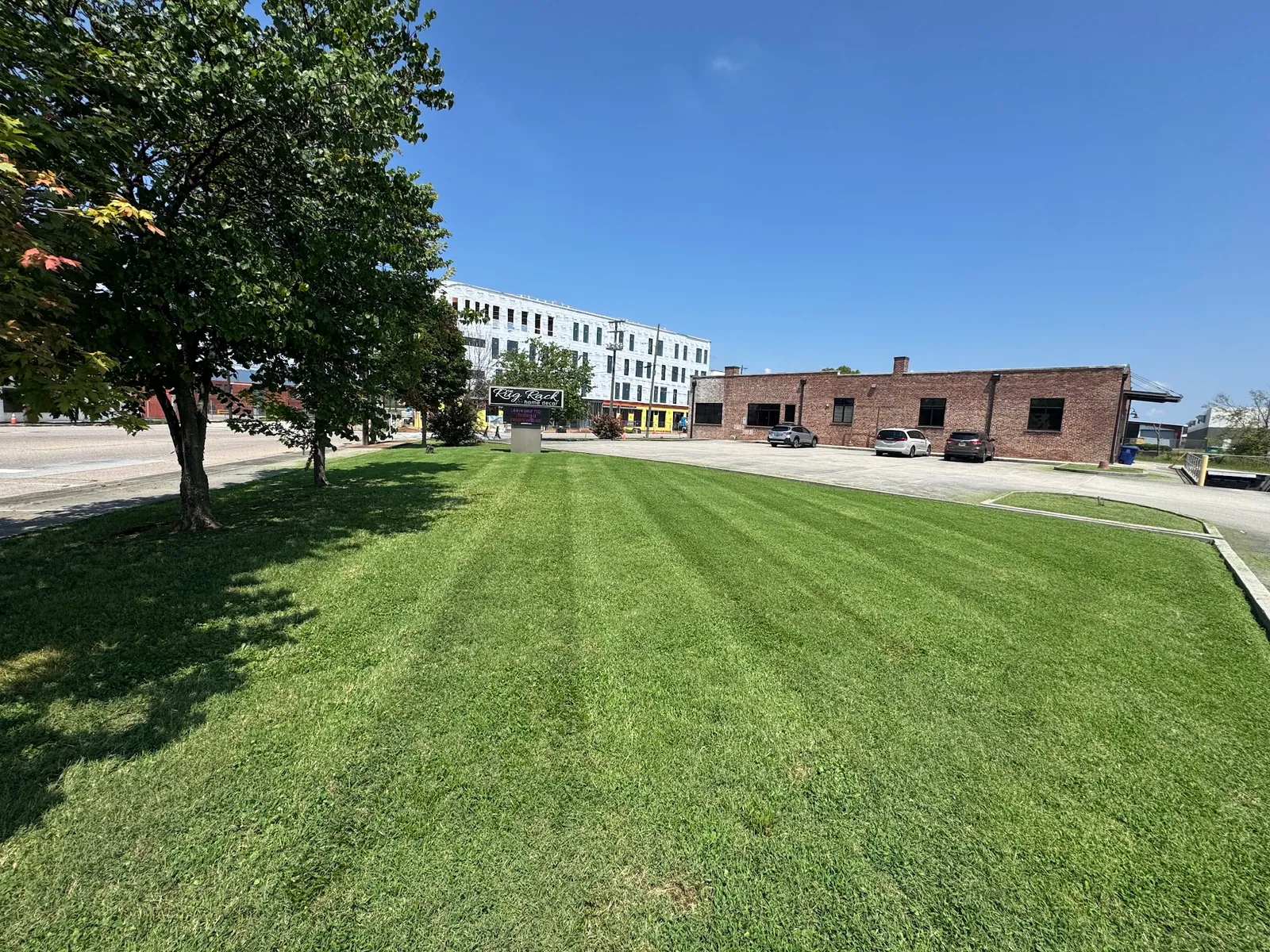 Striped lawn on a commercial property with shade trees and brick buildings behind it