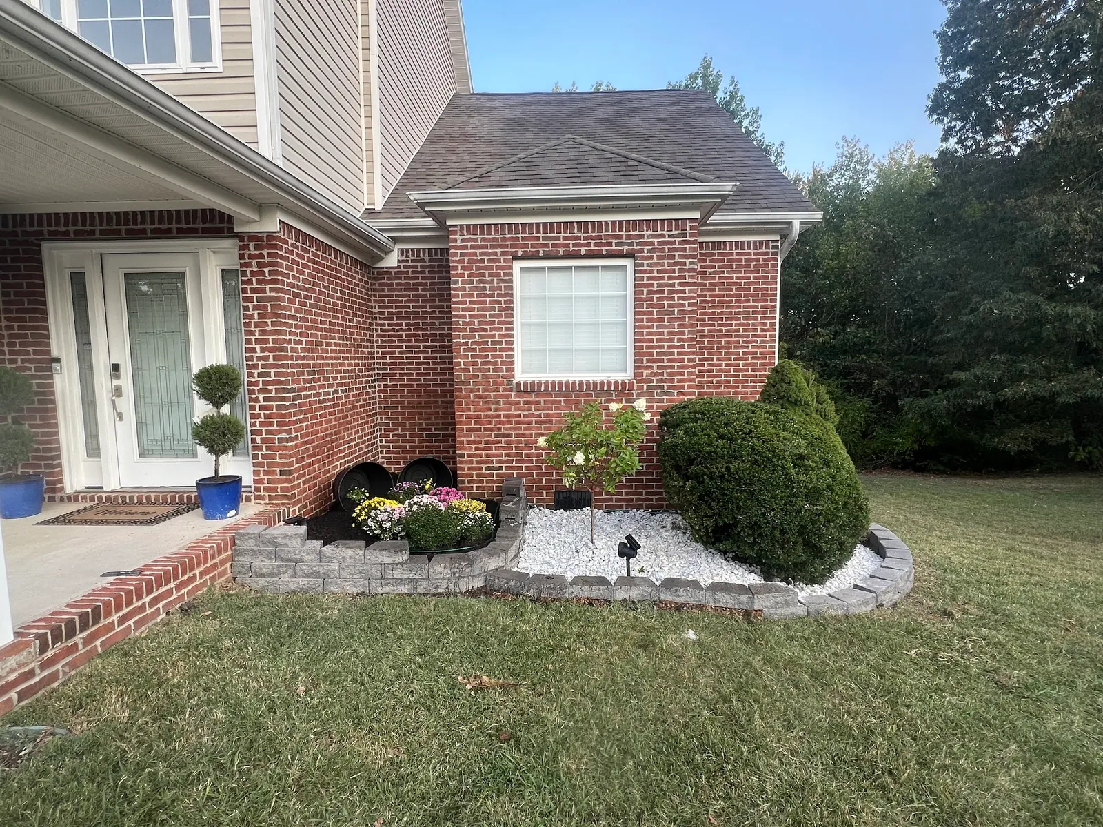 Front landscaping bed with a stone block border, white rock, trimmed shrubs and flowers beside a brick home